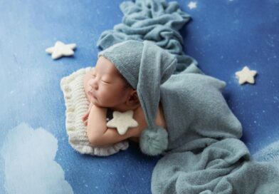 Bebê dormindo tranquilamente com manta e gorro azul em cenário com estrelas, representando conforto, aconchego e dicas para fazer bebê dormir melhor.